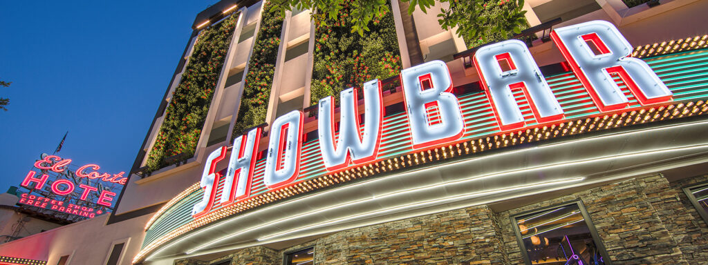Neon signs for SHOWBAR and El Cortez Hotel light up a city street at dusk.