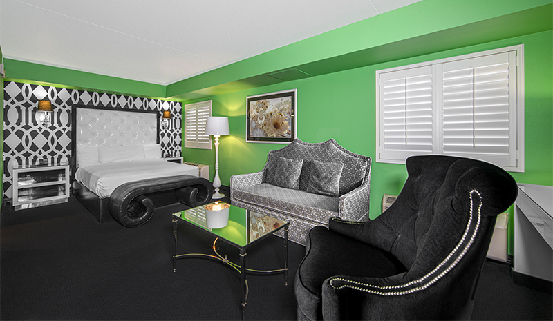 Bright green-walled hotel room with a bed, sofa, armchair, glass table, modern decor, and spacious rooms designed for comfort.