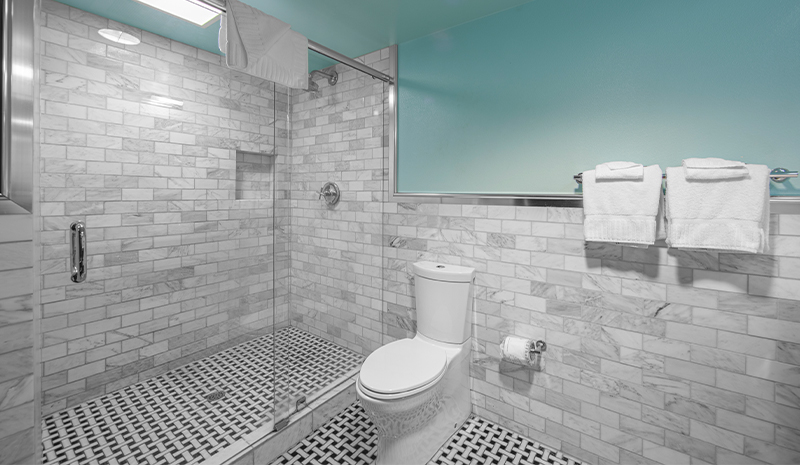 Modern bathroom with a glass shower, white toilet, and towels on a rack, all with tile walls and floor—an inviting space that stands out among contemporary rooms.