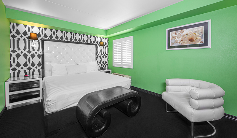 Modern hotel rooms feature a king bed, white headboard, green walls, and unique black-and-white decor.