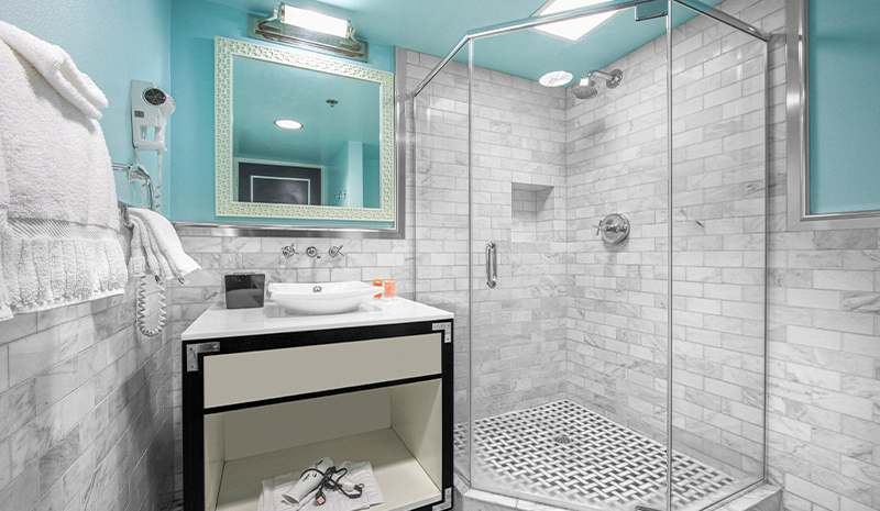 Modern bathroom with glass shower, white sink, towels, and large mirror creates one of the most stylish rooms, featuring elegant marble-patterned walls and floor.