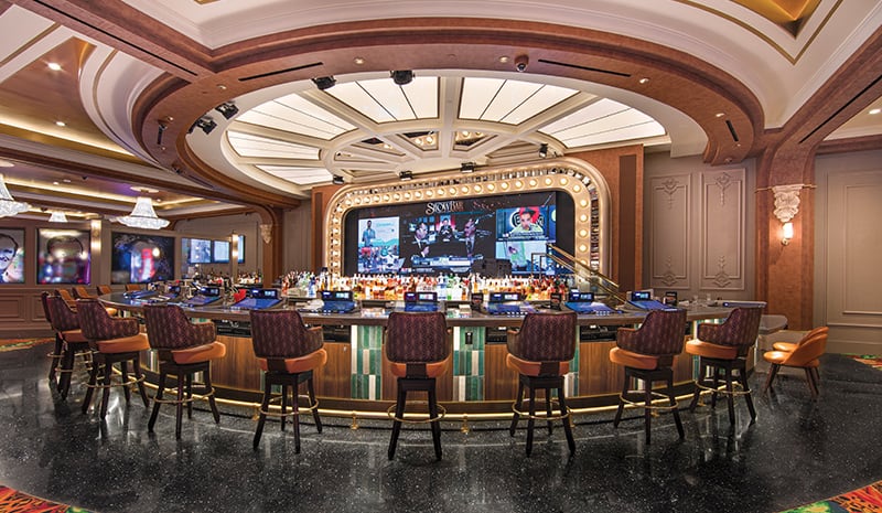 Luxurious casino bar with empty chairs, stocked shelves, and large TV screens under elegant lighting—perfect for guests coming from the nearby rooms to unwind in style.