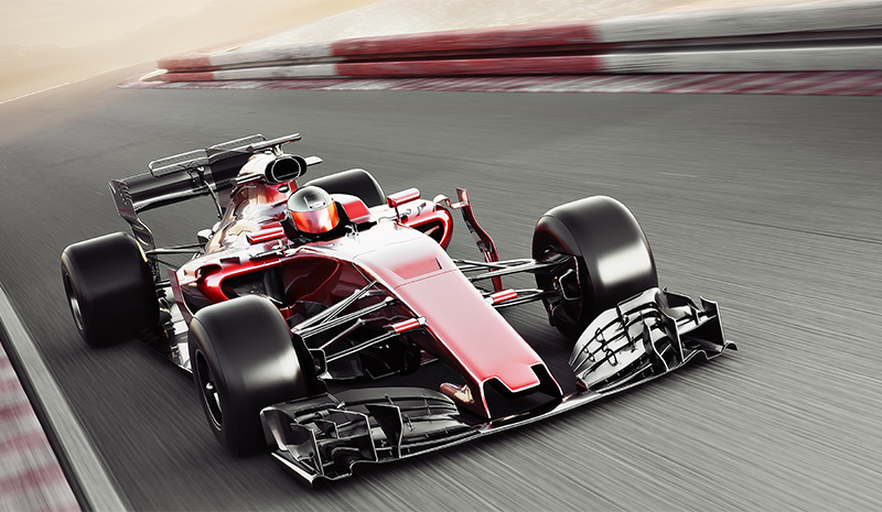 Red Formula 1 race car speeding around a curve, racing past pit rooms with a dynamic blurred motion effect.
